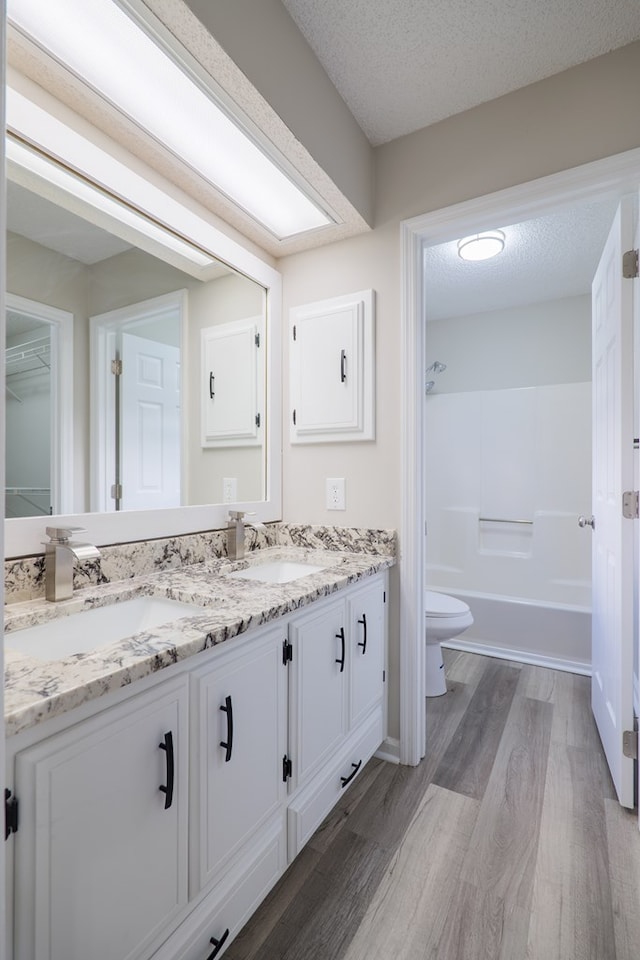 full bathroom featuring shower / bath combination, vanity, a textured ceiling, hardwood / wood-style flooring, and toilet