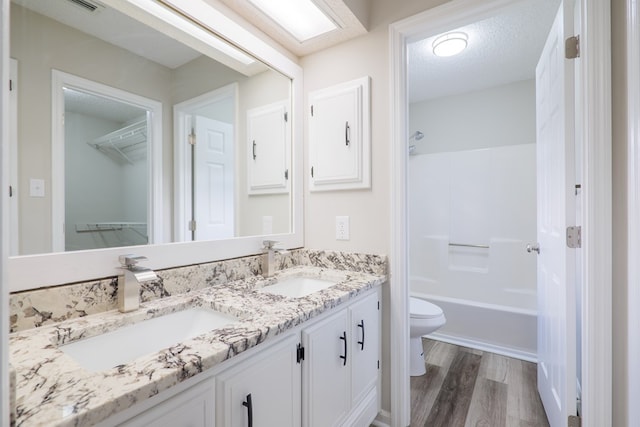 full bathroom with shower / bathtub combination, vanity, a textured ceiling, wood-type flooring, and toilet