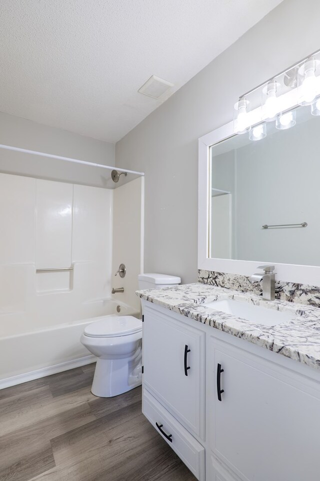 full bathroom with wood-type flooring, a textured ceiling, toilet, vanity, and shower / bathtub combination