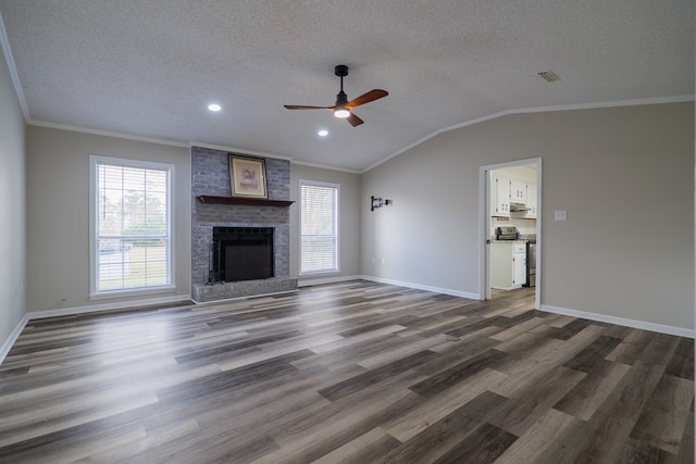 unfurnished living room with a textured ceiling, ornamental molding, dark wood-type flooring, and a brick fireplace