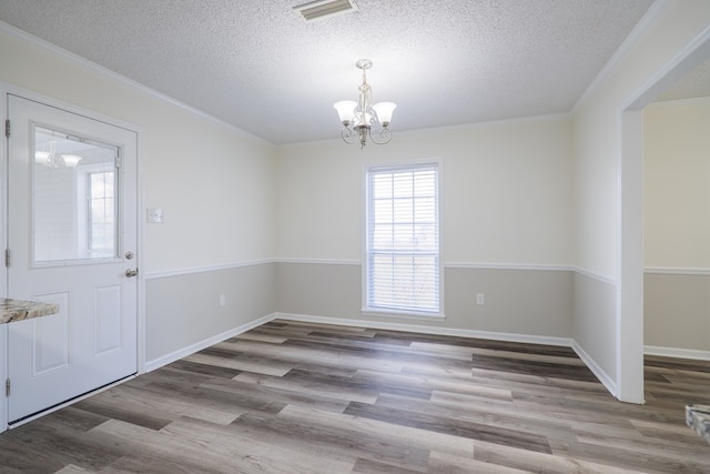 unfurnished dining area with a textured ceiling, light wood-type flooring, crown molding, and a chandelier