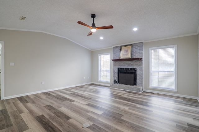 unfurnished living room featuring lofted ceiling, a brick fireplace, ornamental molding, light wood-type flooring, and a textured ceiling