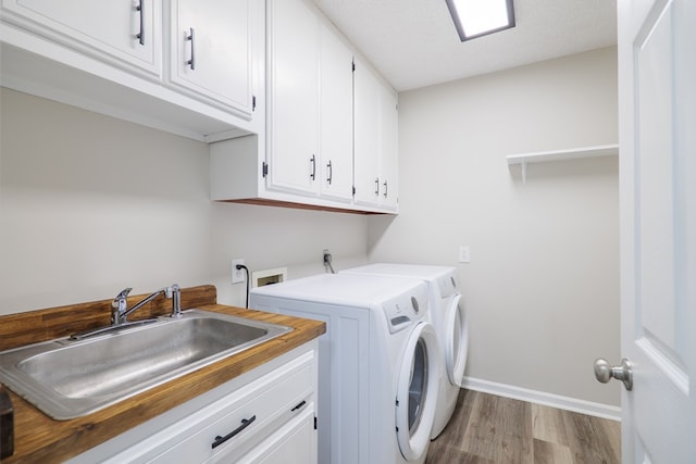 washroom with cabinets, a textured ceiling, washer and clothes dryer, sink, and light hardwood / wood-style floors