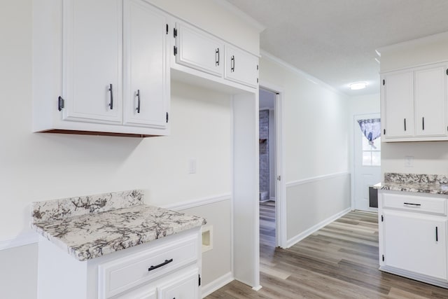 kitchen with white cabinets, light wood-type flooring, light stone counters, and crown molding