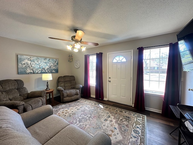 living area featuring baseboards, a ceiling fan, dark wood-style flooring, and a textured ceiling