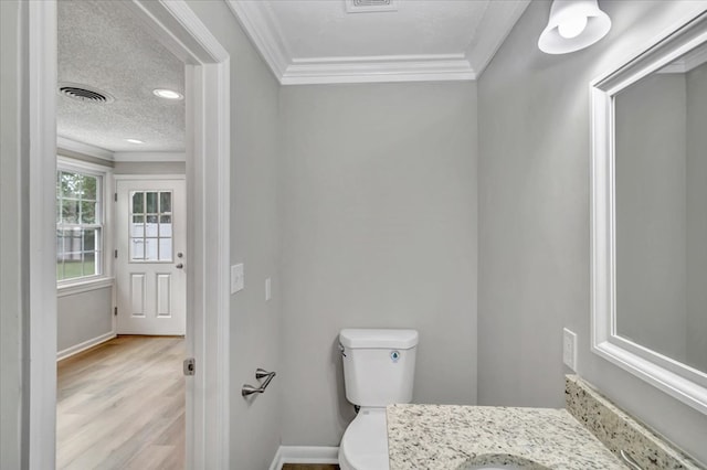 bathroom featuring wood-type flooring, a textured ceiling, toilet, vanity, and ornamental molding