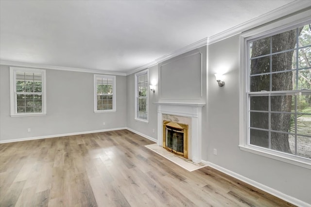 unfurnished living room featuring a fireplace, a healthy amount of sunlight, light wood-type flooring, and ornamental molding