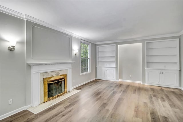 unfurnished living room featuring built in shelves, a premium fireplace, light hardwood / wood-style flooring, and ornamental molding