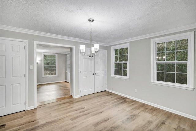 unfurnished dining area featuring light hardwood / wood-style flooring, a chandelier, a textured ceiling, and ornamental molding