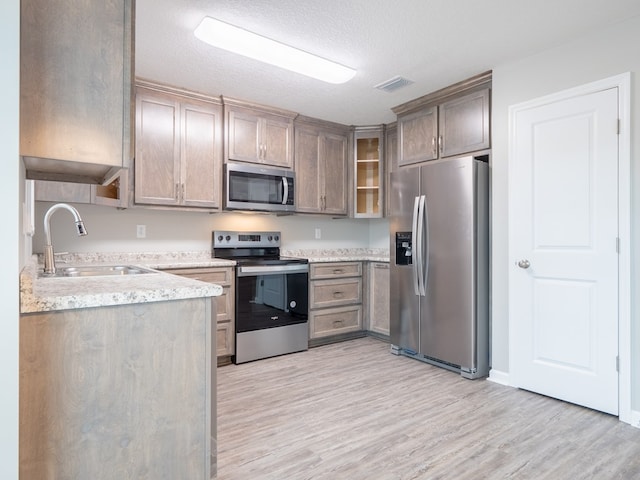 kitchen with a textured ceiling, stainless steel appliances, light hardwood / wood-style floors, and sink