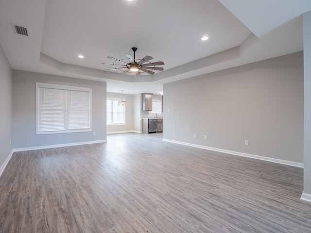 unfurnished living room with ceiling fan with notable chandelier, a raised ceiling, and wood-type flooring