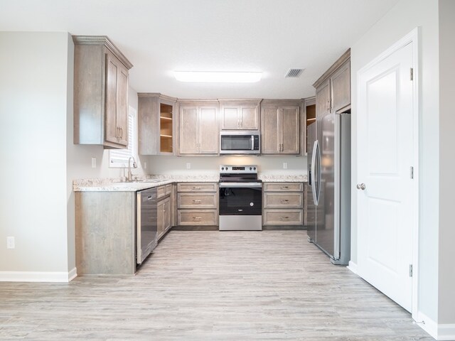 kitchen with light stone countertops, sink, stainless steel appliances, and light hardwood / wood-style floors