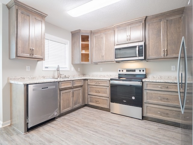 kitchen featuring light stone counters, a textured ceiling, stainless steel appliances, sink, and light hardwood / wood-style floors