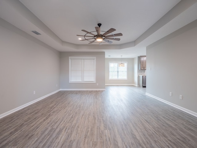 unfurnished living room featuring hardwood / wood-style flooring, ceiling fan with notable chandelier, and a raised ceiling