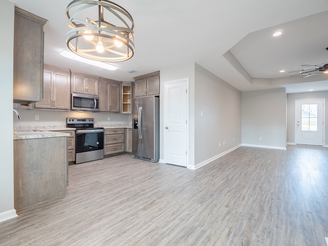 kitchen featuring appliances with stainless steel finishes, light stone counters, ceiling fan with notable chandelier, sink, and light hardwood / wood-style floors