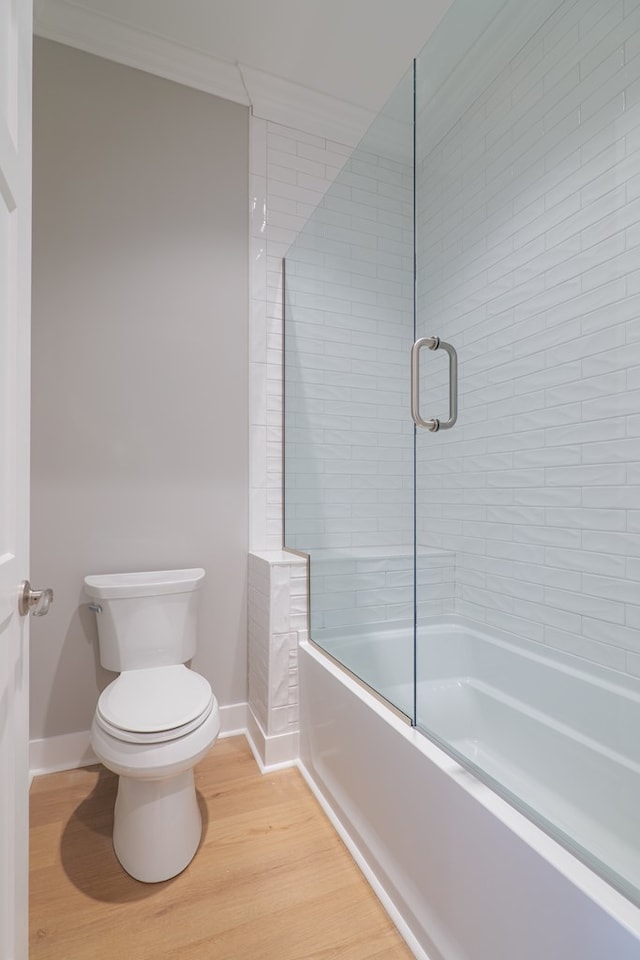 bathroom with hardwood / wood-style flooring, bath / shower combo with glass door, ornamental molding, and toilet