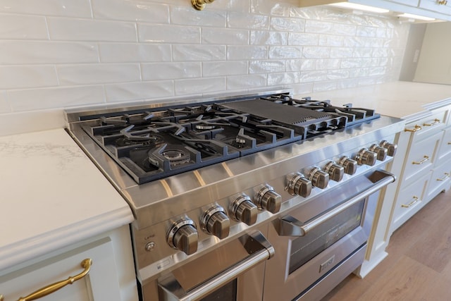 interior details featuring tasteful backsplash, white cabinetry, double oven range, light stone counters, and light hardwood / wood-style flooring