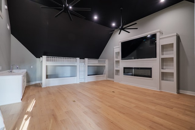 unfurnished living room with built in shelves, sink, vaulted ceiling, ceiling fan, and light hardwood / wood-style floors