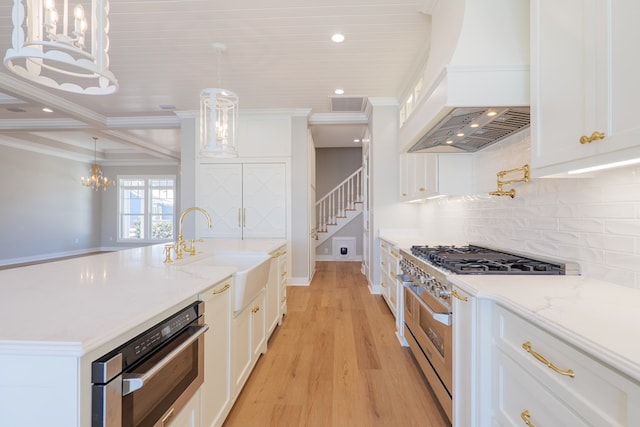 kitchen featuring high end stove, sink, white cabinets, custom exhaust hood, and hanging light fixtures