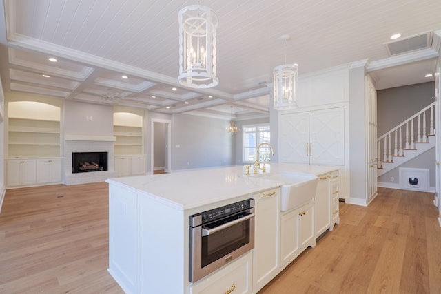 kitchen featuring pendant lighting, sink, coffered ceiling, a center island with sink, and stainless steel oven