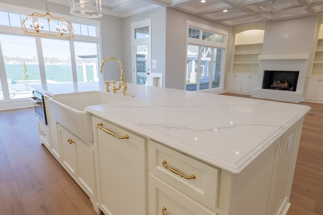 kitchen with sink, hanging light fixtures, coffered ceiling, a water view, and light stone countertops