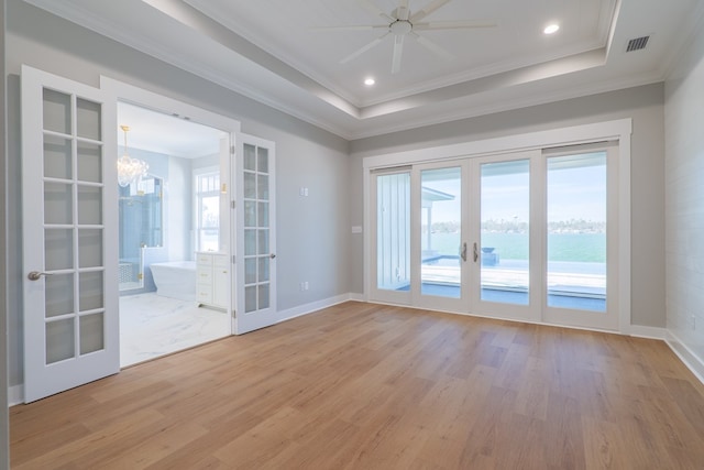 spare room with a raised ceiling, crown molding, light wood-type flooring, and french doors