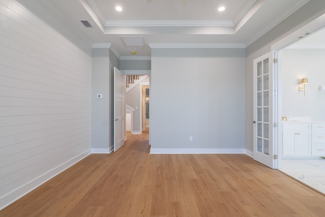 spare room featuring crown molding, wooden walls, light hardwood / wood-style floors, and a raised ceiling