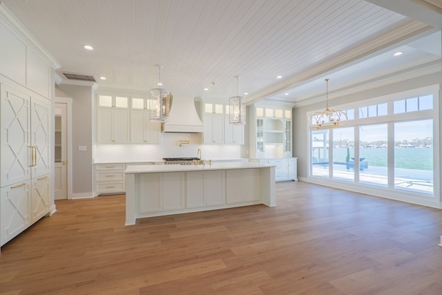 kitchen with white cabinetry, custom exhaust hood, ornamental molding, hanging light fixtures, and a water view