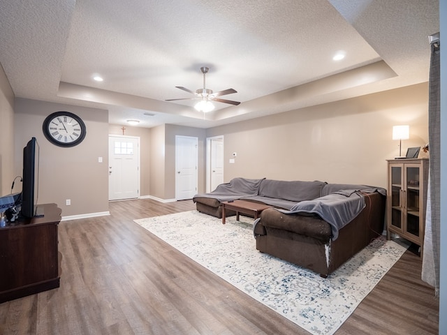 living room featuring a raised ceiling, wood finished floors, baseboards, and a textured ceiling