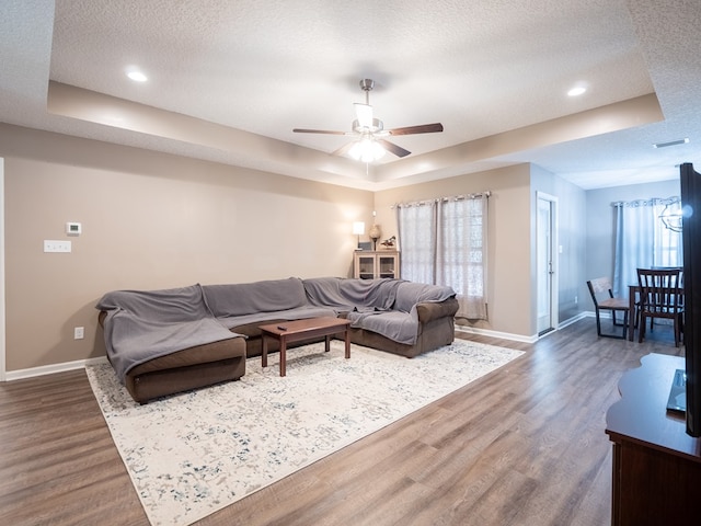 living room with a raised ceiling, wood finished floors, baseboards, and a textured ceiling