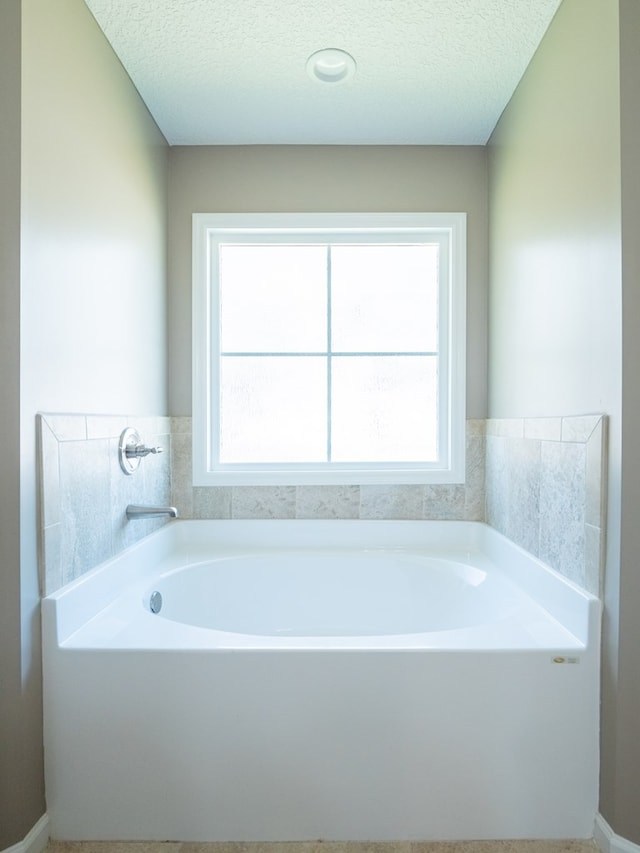 bathroom featuring a garden tub, a healthy amount of sunlight, and a textured ceiling