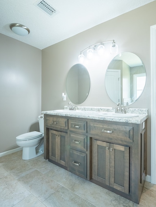 bathroom with double vanity, visible vents, toilet, and a sink