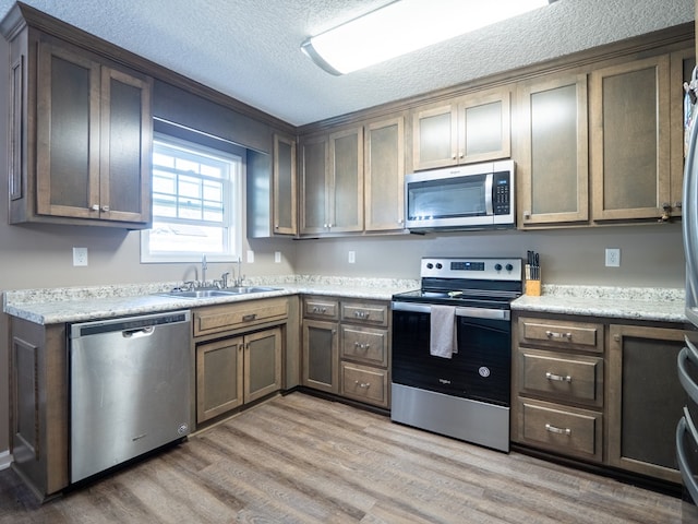 kitchen featuring light countertops, stainless steel appliances, light wood-style floors, a textured ceiling, and a sink