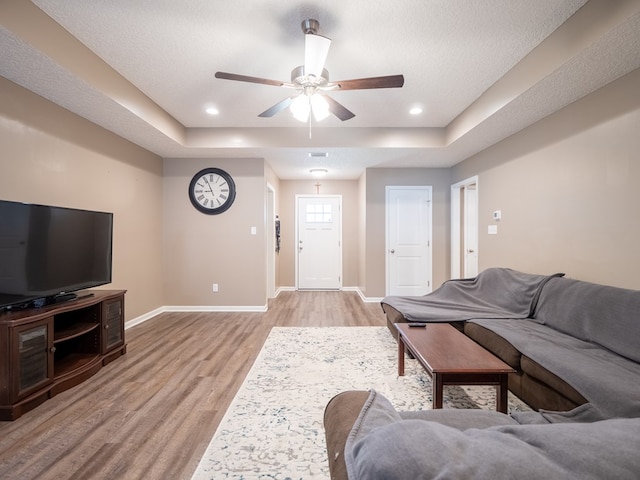 living area featuring light wood-type flooring, a tray ceiling, baseboards, and recessed lighting