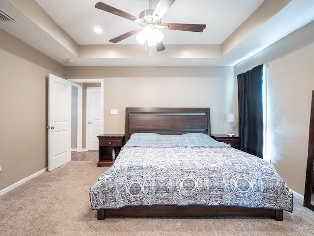 carpeted bedroom featuring visible vents, ceiling fan, baseboards, and a tray ceiling