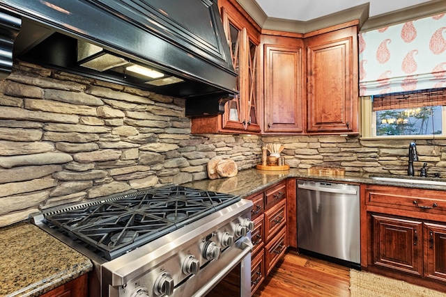 kitchen featuring sink, appliances with stainless steel finishes, custom range hood, dark stone counters, and light hardwood / wood-style floors