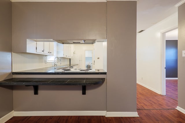 kitchen featuring dark hardwood / wood-style flooring, a kitchen breakfast bar, kitchen peninsula, washer / clothes dryer, and white cabinets