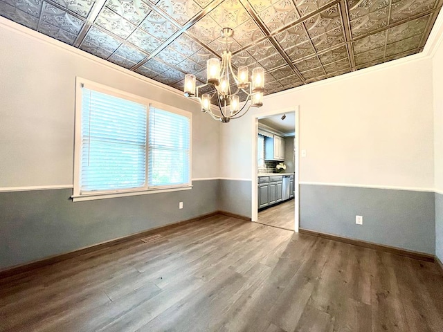 unfurnished dining area with ornamental molding, wood-type flooring, and an inviting chandelier