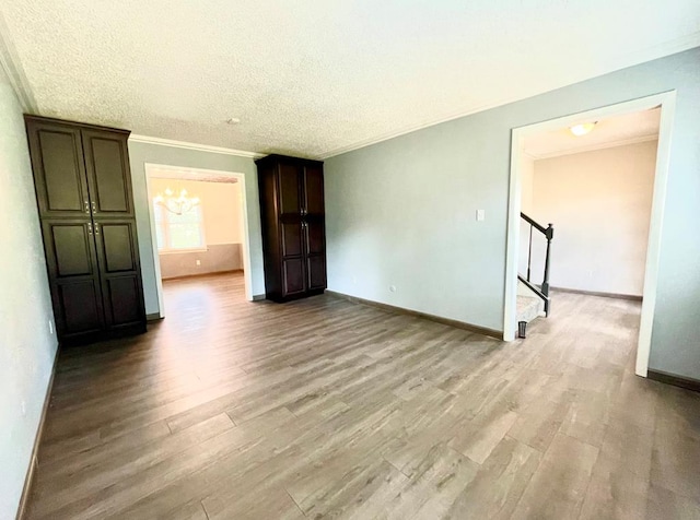 unfurnished room with crown molding, a textured ceiling, a notable chandelier, and light wood-type flooring