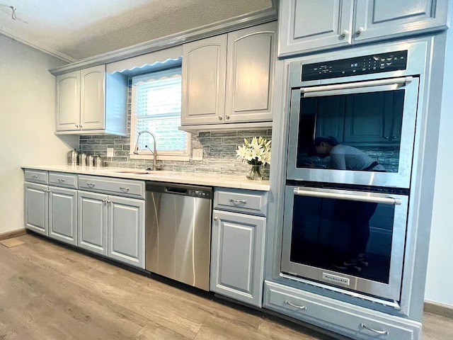 kitchen with sink, gray cabinets, backsplash, stainless steel appliances, and light wood-type flooring