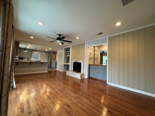 unfurnished living room with built in shelves, ornamental molding, wood-type flooring, and a brick fireplace