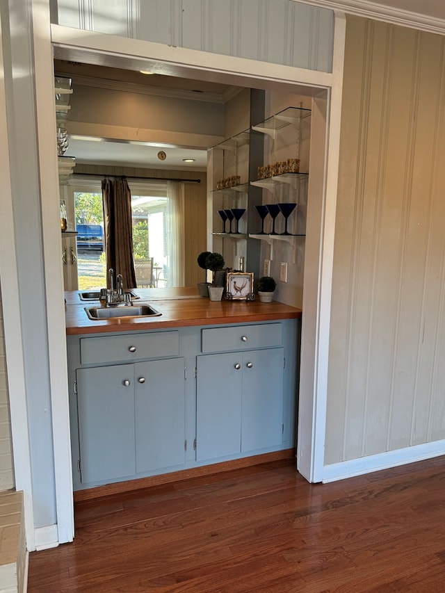 bar featuring dark wood-type flooring, butcher block countertops, ornamental molding, and sink