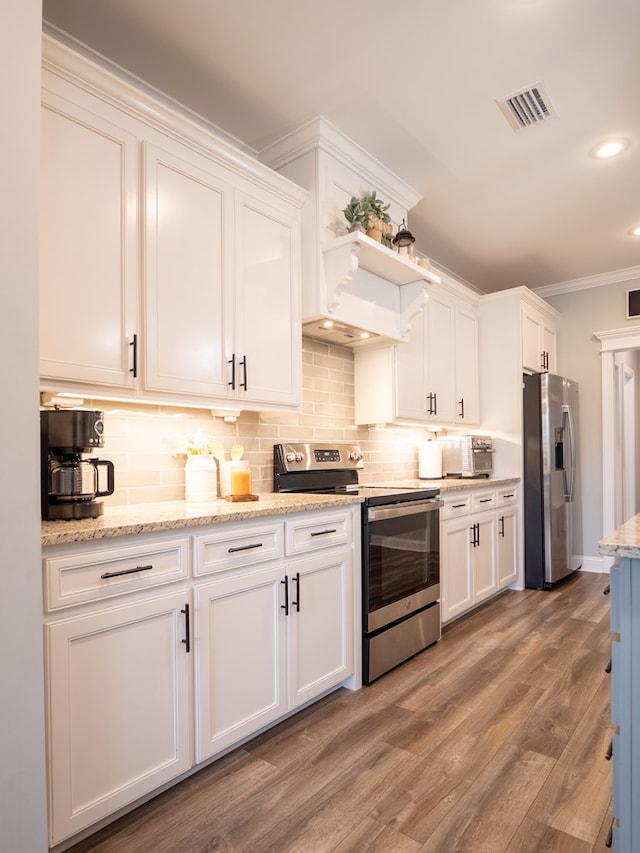 kitchen with light wood-type flooring, ornamental molding, appliances with stainless steel finishes, white cabinets, and backsplash