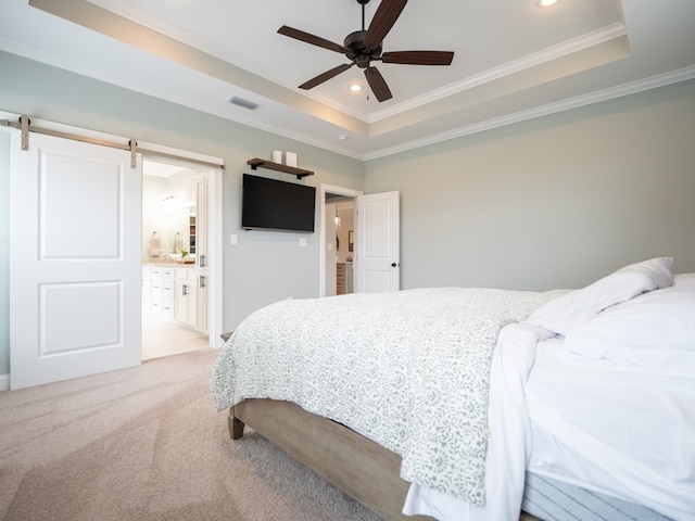 carpeted bedroom with a tray ceiling, ornamental molding, a barn door, and ensuite bathroom