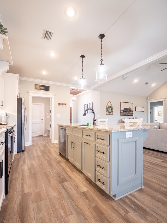 kitchen with an island with sink, white cabinets, hanging light fixtures, light stone counters, and stainless steel appliances