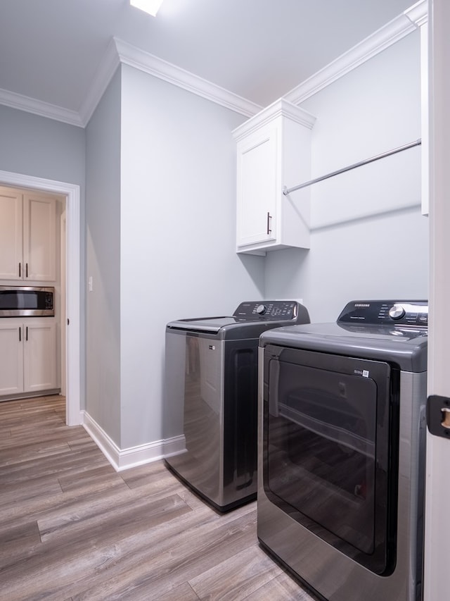 laundry area featuring cabinets, independent washer and dryer, crown molding, and light hardwood / wood-style flooring