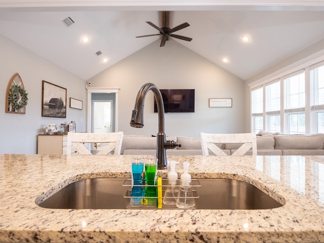 kitchen with lofted ceiling, sink, light stone countertops, and ceiling fan