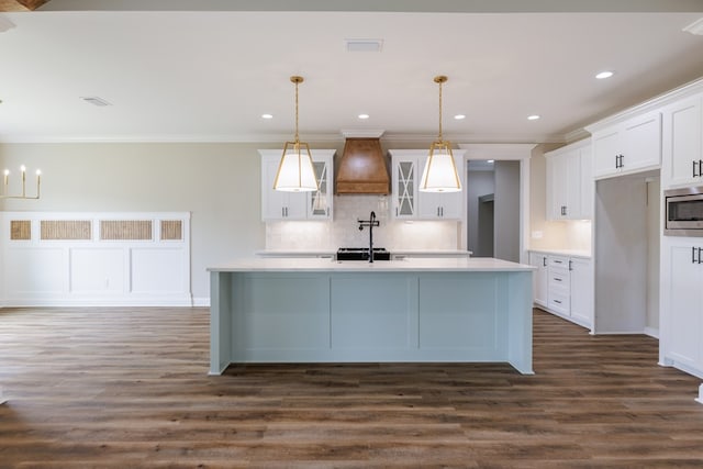 3061 Houser Way, Hahira, GA 31632 - kitchen featuring custom range hood, stainless steel microwave, light countertops, tasteful backsplash, and an island with sink