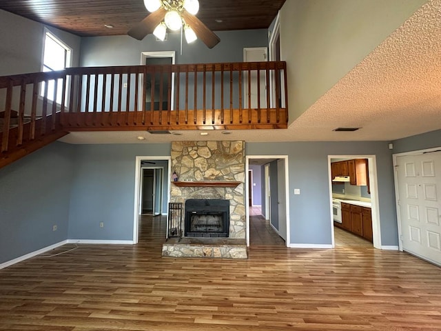 unfurnished living room featuring a towering ceiling, a stone fireplace, hardwood / wood-style floors, and wooden ceiling