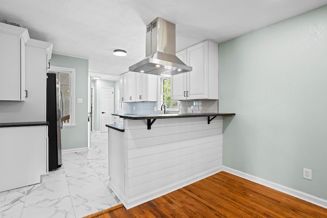 kitchen with freestanding refrigerator, dark countertops, island range hood, and white cabinets